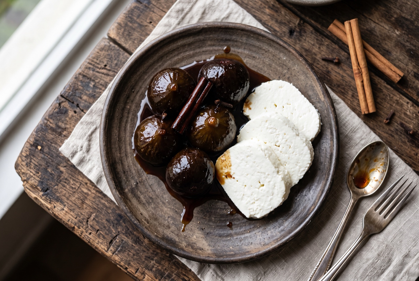 Dark candied figs glistening in panela syrup in a bowl, with a thick slice of white fresh cheese beside them