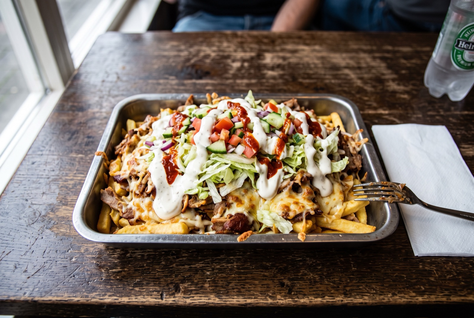 Tray of fries topped with shawarma meat and melted Gouda, piled with shredded lettuce, tomato and garlic sauce