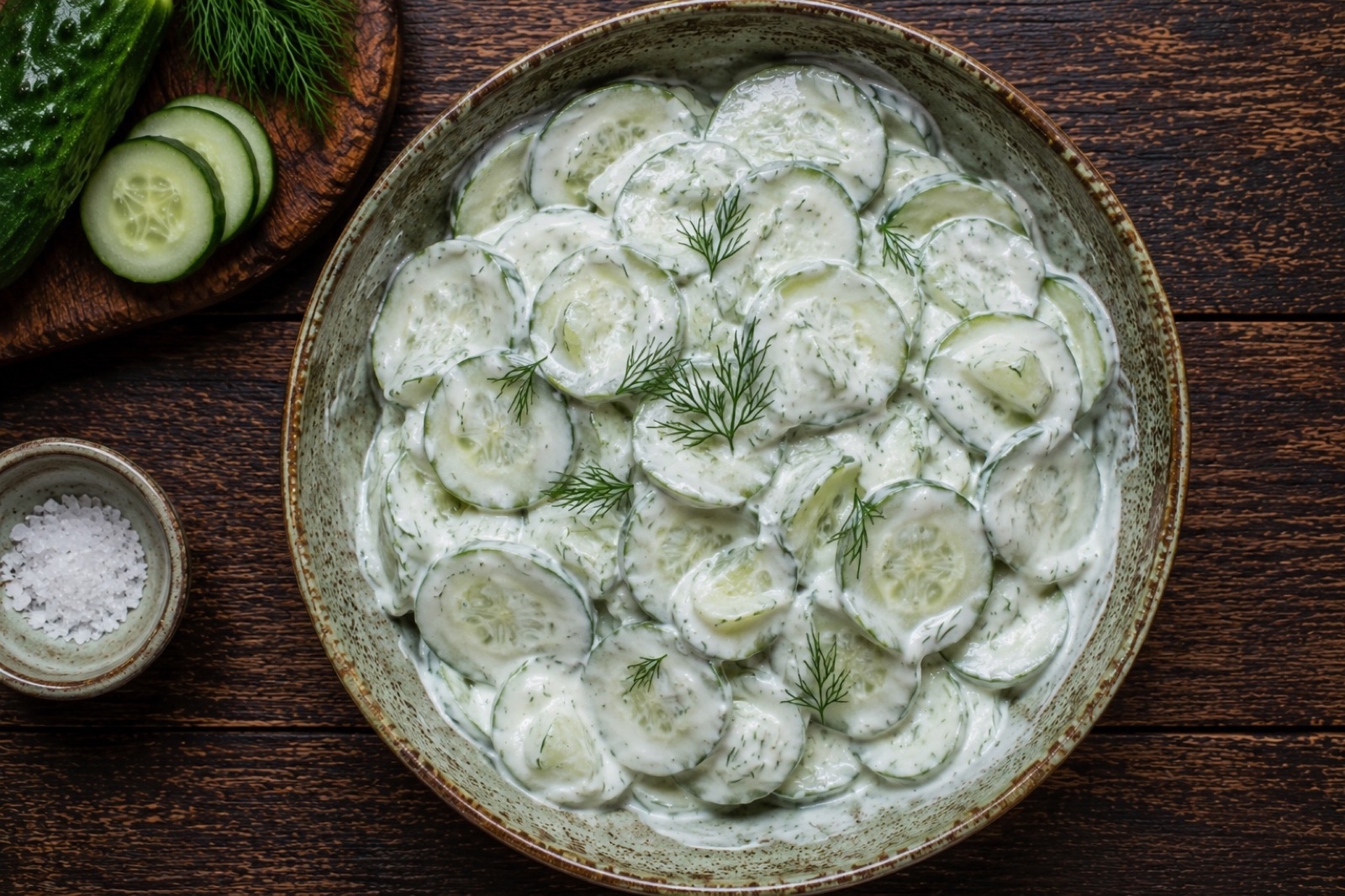 Bowl of Polish cucumber salad, thin slices coated in sour cream dressing and scattered with chopped dill