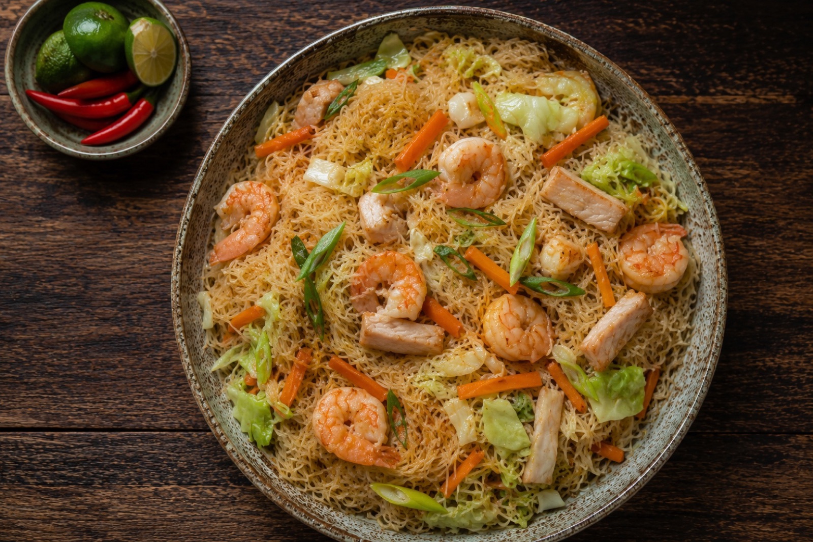 Platter of pancit bihon rice noodles with shrimp, chicken strips, carrot matchsticks and cabbage, calamansi wedges alongside