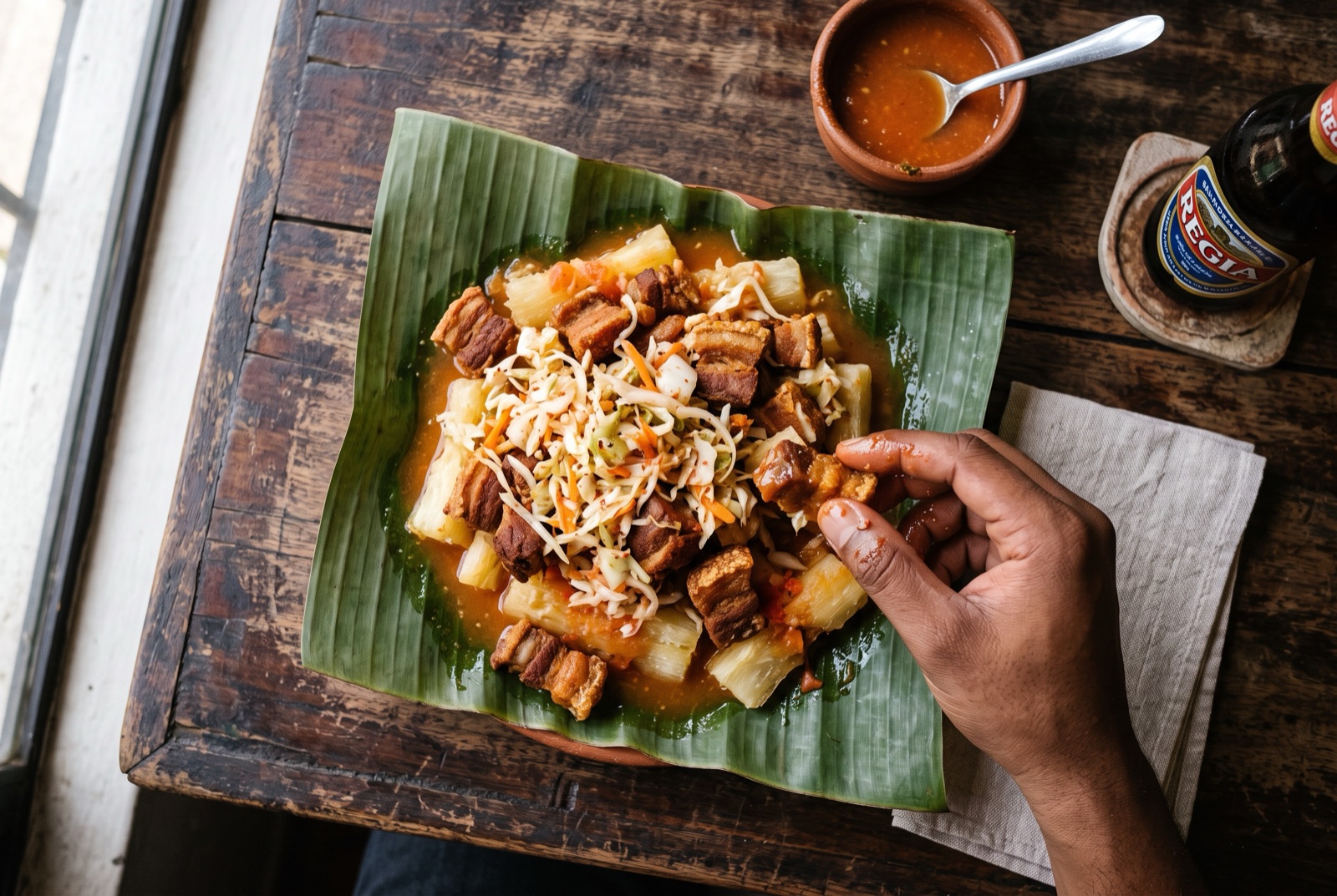 Boiled cassava chunks topped with crackling fried pork and curtido on a banana leaf, tomato salsa poured over