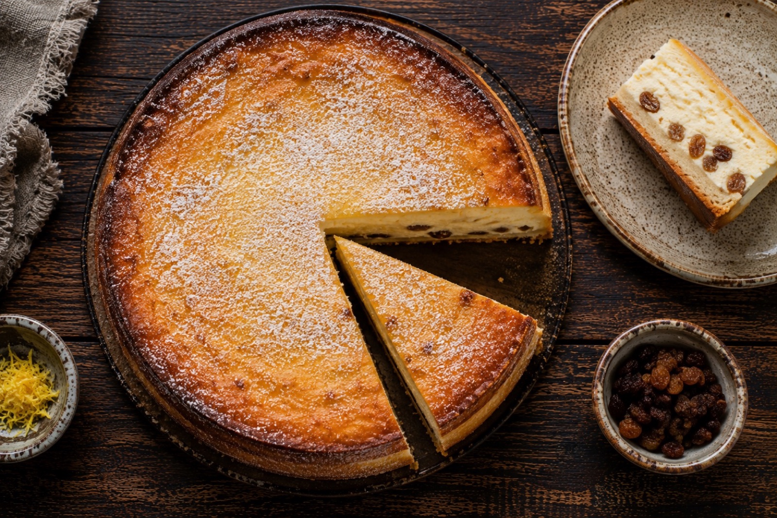 Slice of Polish sernik showing dense pale curd filling with raisins on a thin golden shortcrust base