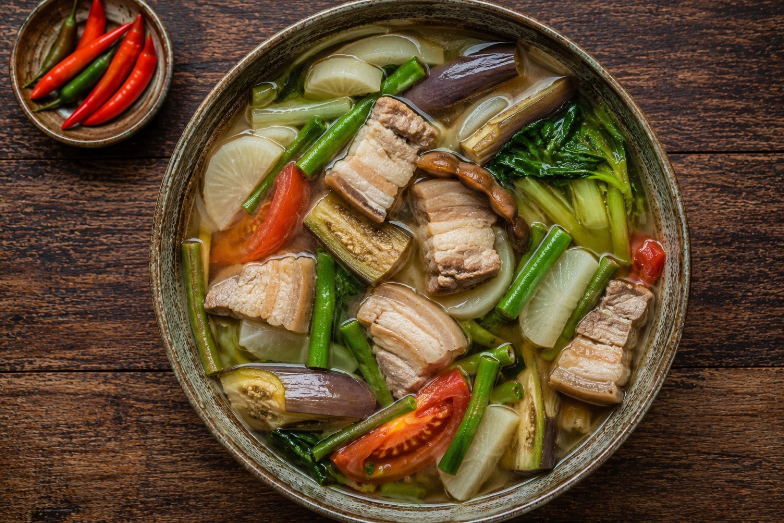 Steaming bowl of sinigang na baboy with pork belly, daikon, okra and water spinach in clear sour tamarind broth